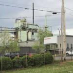 Industrial facility with ExxonMobil sign, large green processing buildings, and a chain-link fence in foreground under cloudy sky