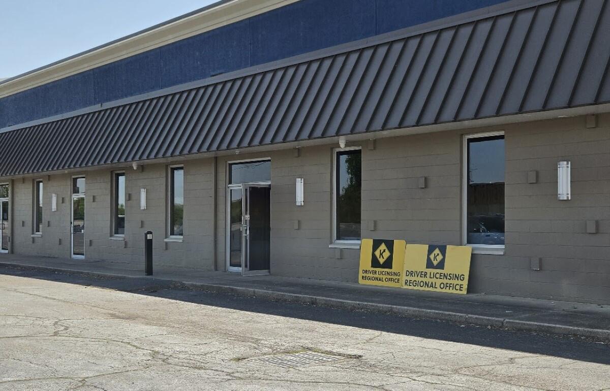 Exterior view of a beige office building with a blue upper trim and diagonal metal awning, near two Driver Licensing Regional Office signs outside the entrance.