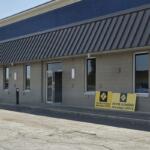 Exterior view of a beige office building with a blue upper trim and diagonal metal awning, near two Driver Licensing Regional Office signs outside the entrance.