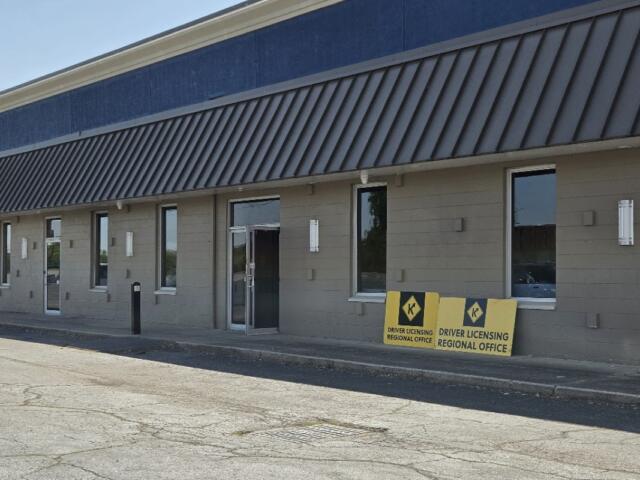 Exterior view of a beige office building with a blue upper trim and diagonal metal awning, near two Driver Licensing Regional Office signs outside the entrance.
