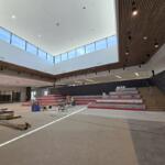 Interior of a modern auditorium under renovation with red tiered seating being installed and tools on the floor