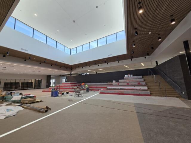 Interior of a modern auditorium under renovation with red tiered seating being installed and tools on the floor