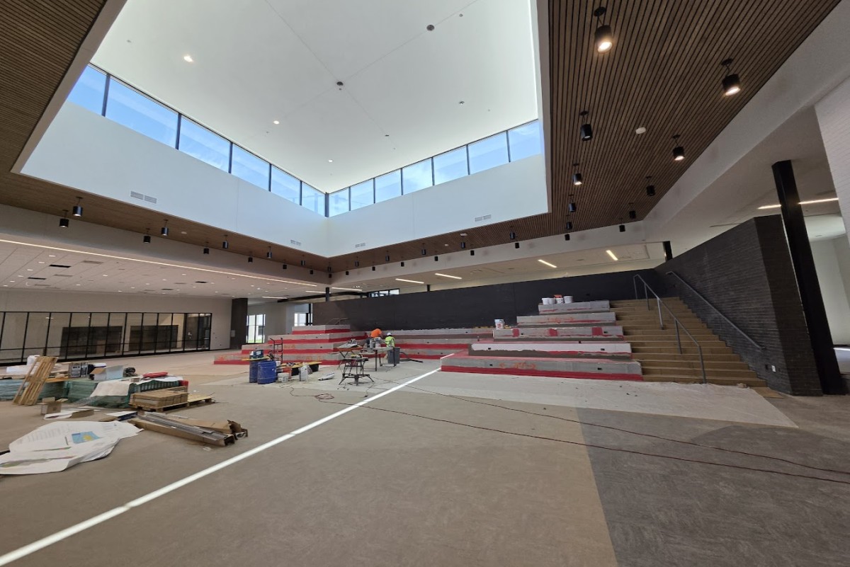 Interior of a modern auditorium under renovation with red tiered seating being installed and tools on the floor