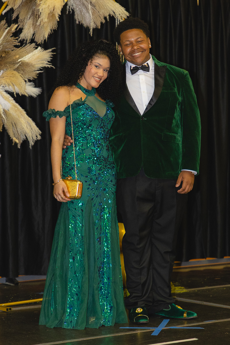 Two young adults in formal attire posing together on a stage, smiling at the camera.