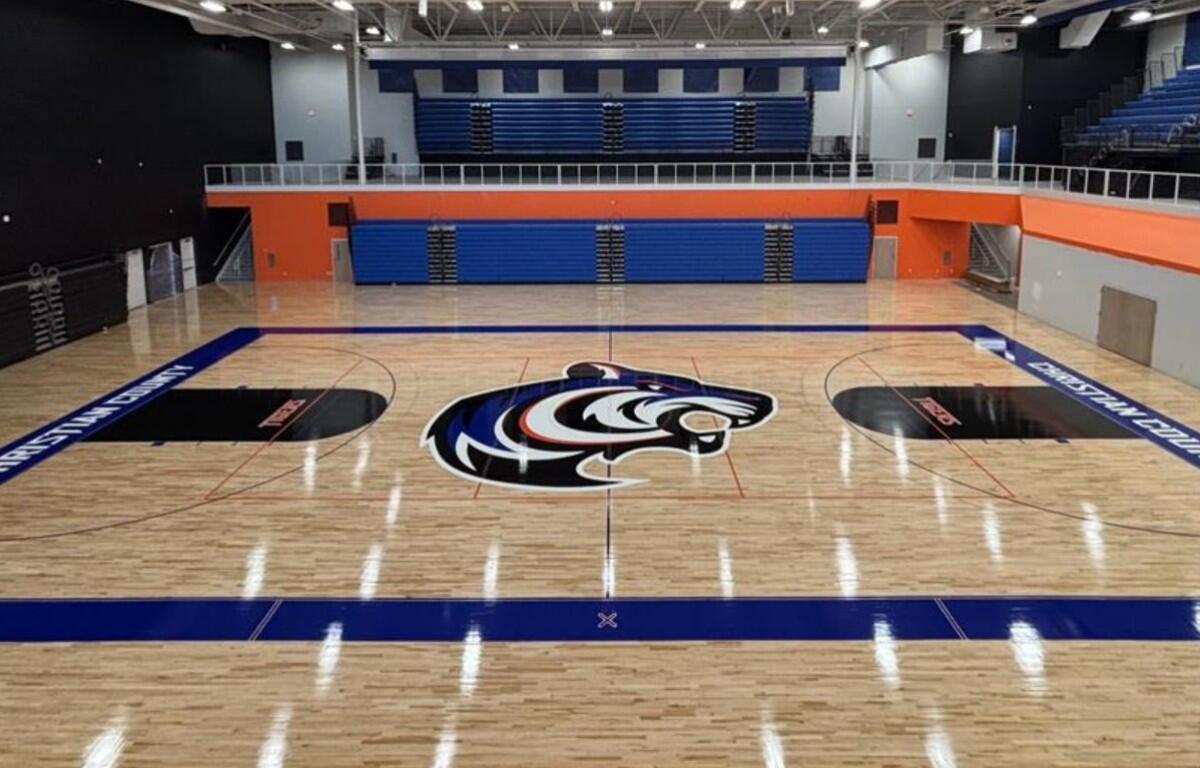 Empty indoor basketball court with a large tiger logo at center and blue bleachers in the background.