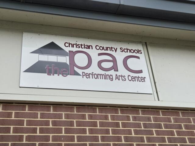Sign reading 'Christian County Schools PAC' and 'Performing Arts Center' with a building logo on a white plaque above a brick wall