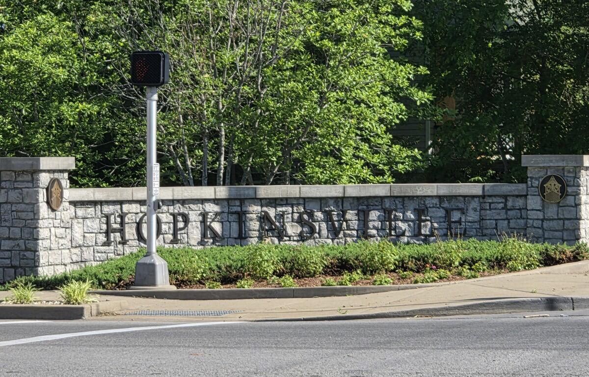 Stone wall sign reading 'Hopkinsville' with shrubs and a small traffic signal in front.