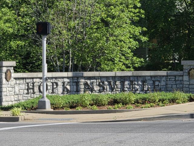 Stone wall sign reading 'Hopkinsville' with shrubs and a small traffic signal in front.