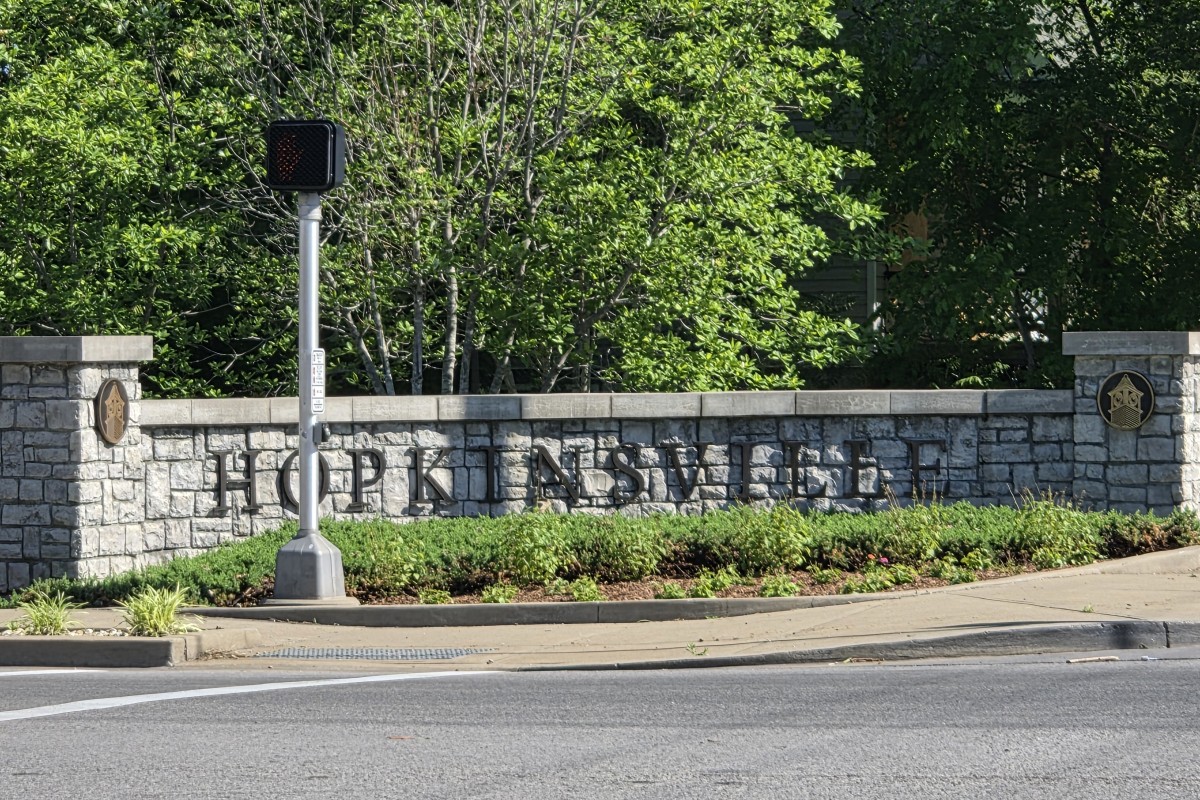 Stone wall sign reading 'Hopkinsville' with shrubs and a small traffic signal in front.