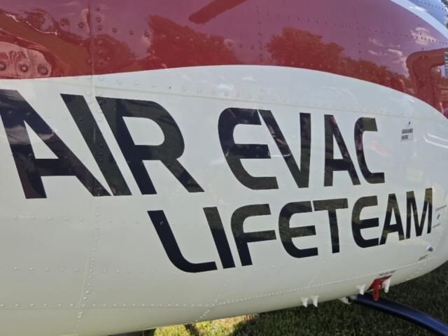 Helicopter fuselage with bold black lettering reading 'AIR EVAC LIFETEAM' on a white and red body, parked on grass.