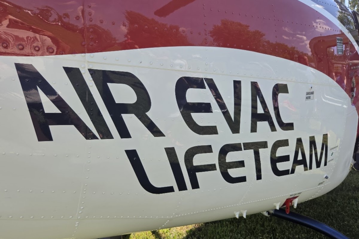 Helicopter fuselage with bold black lettering reading 'AIR EVAC LIFETEAM' on a white and red body, parked on grass.
