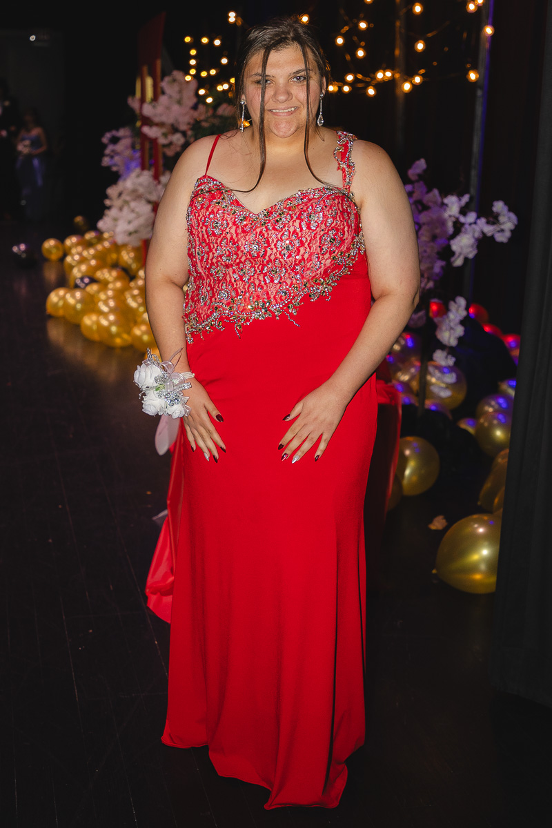 Woman in a red, beaded evening gown posing at a ballroom event with fairy lights in the background.