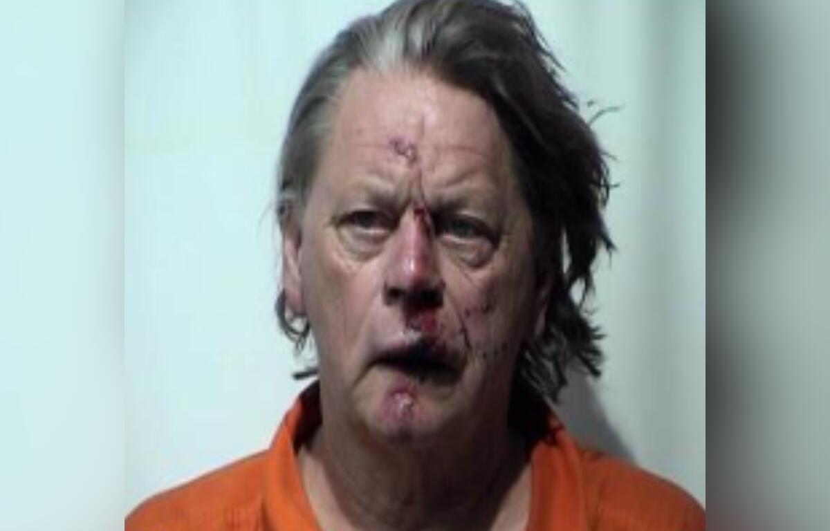 Mugshot of a middle-aged man with bruised, bloodied face wearing an orange prison jumpsuit.