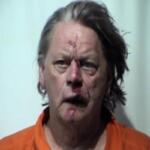 Mugshot of a middle-aged man with bruised, bloodied face wearing an orange prison jumpsuit.