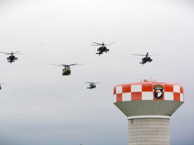 Six helicopters fly in a loose formation above a red-and-white checkered air tower with an Airborne insignia patch at the top.