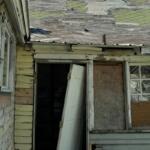 Dilapidated house exterior with peeling paint, an ajar door, and a boarded-up window.