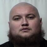 Mugshot of a bald man with a thick beard facing the camera against a plain light background.