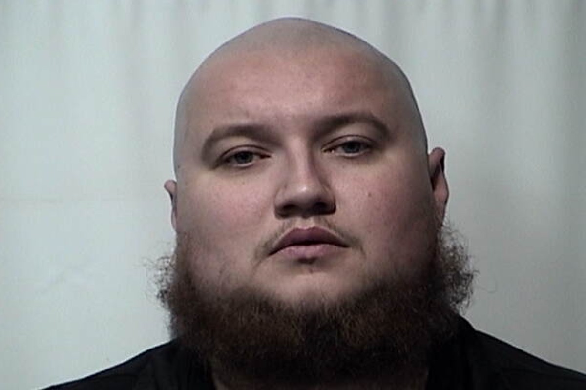 Mugshot of a bald man with a thick beard facing the camera against a plain light background.