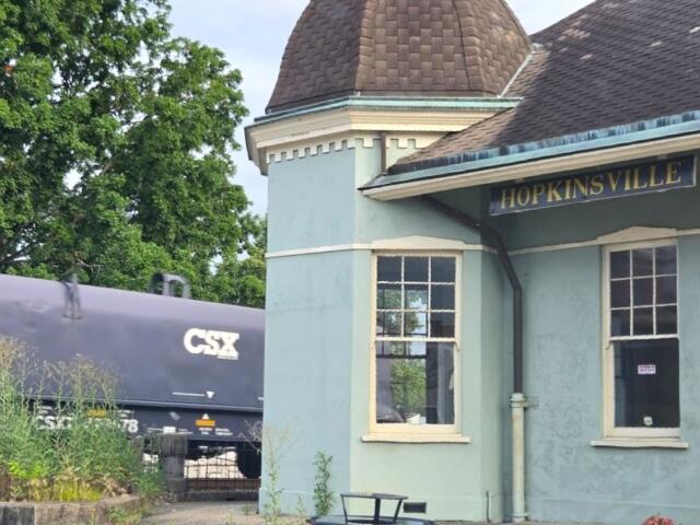 Small blue-green train station with 'HOPKINSVILLE' sign, next to a CSX freight car and rails in the background