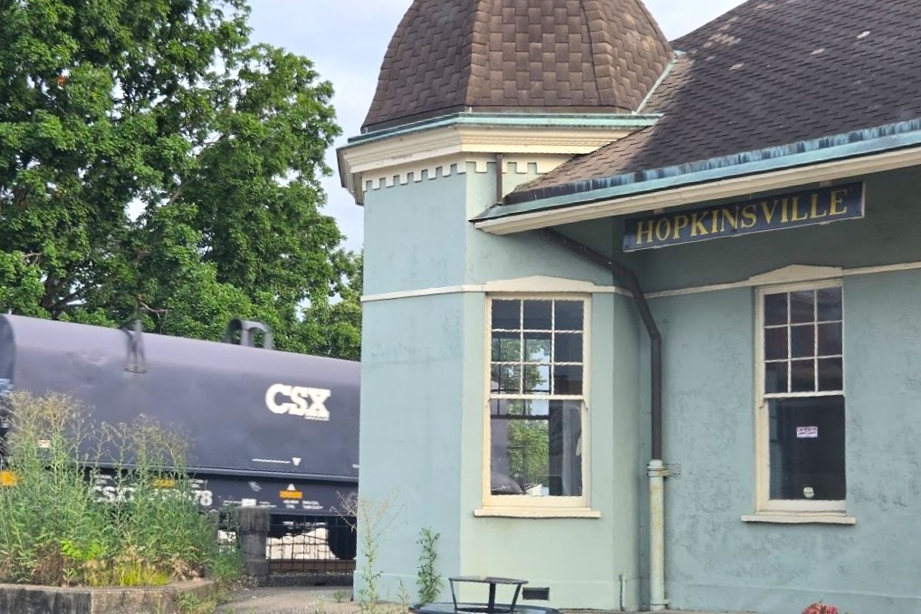 Small blue-green train station with 'HOPKINSVILLE' sign, next to a CSX freight car and rails in the background