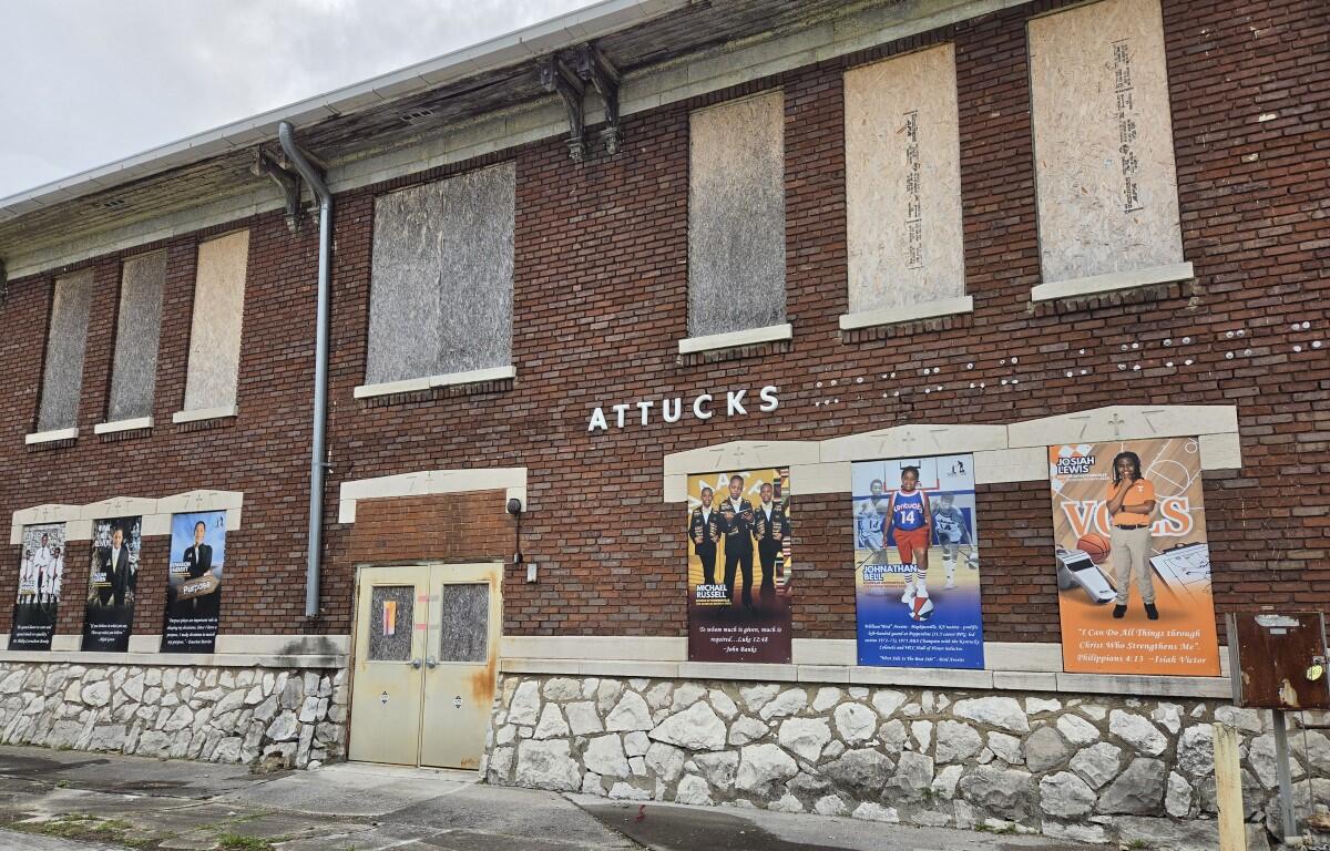 Brick building with boarded-up windows and a stone foundation; posters line the lower wall advertising events or shows.
