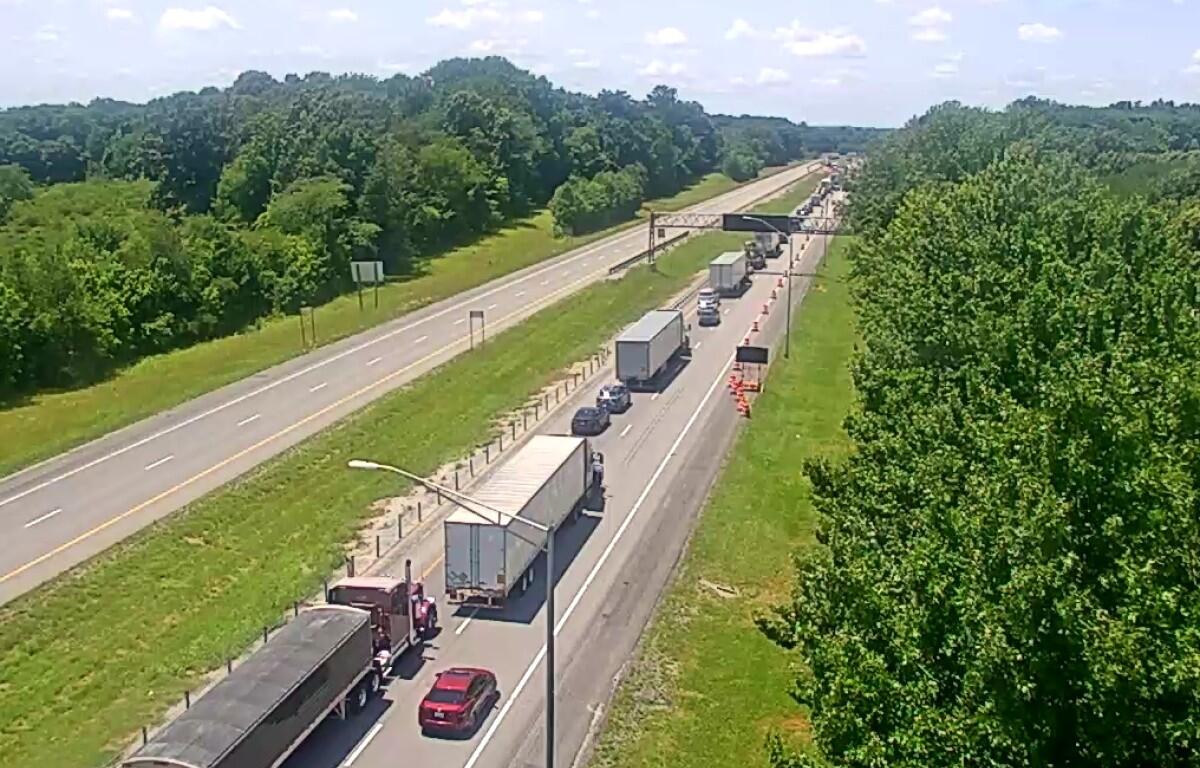 Traffic jam on a highway: multiple trucks and cars lined up in the right lanes near a construction area with orange cones and an overhead sign gantry.