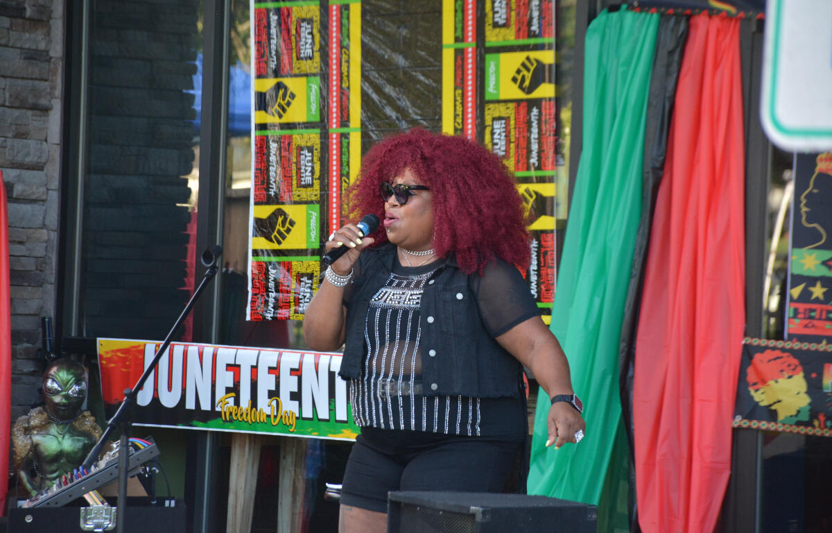 Black woman singer with red curly hair performing on stage at Juneteenth Freedom Day, holding a microphone.