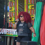 Black woman singer with red curly hair performing on stage at Juneteenth Freedom Day, holding a microphone.