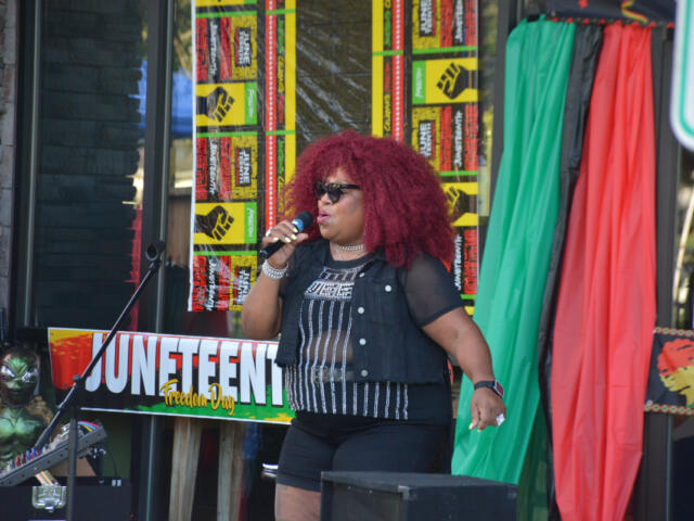 Black woman singer with red curly hair performing on stage at Juneteenth Freedom Day, holding a microphone.