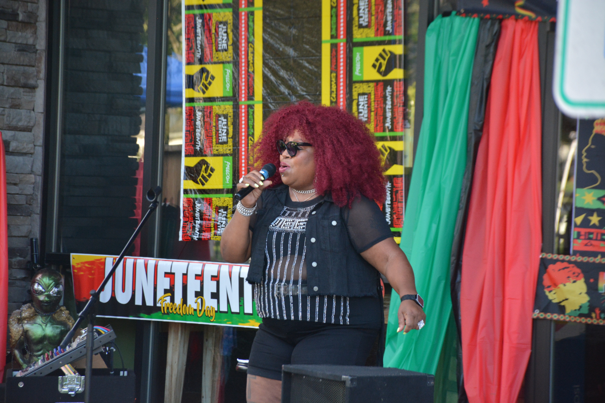 Black woman singer with red curly hair performing on stage at Juneteenth Freedom Day, holding a microphone.
