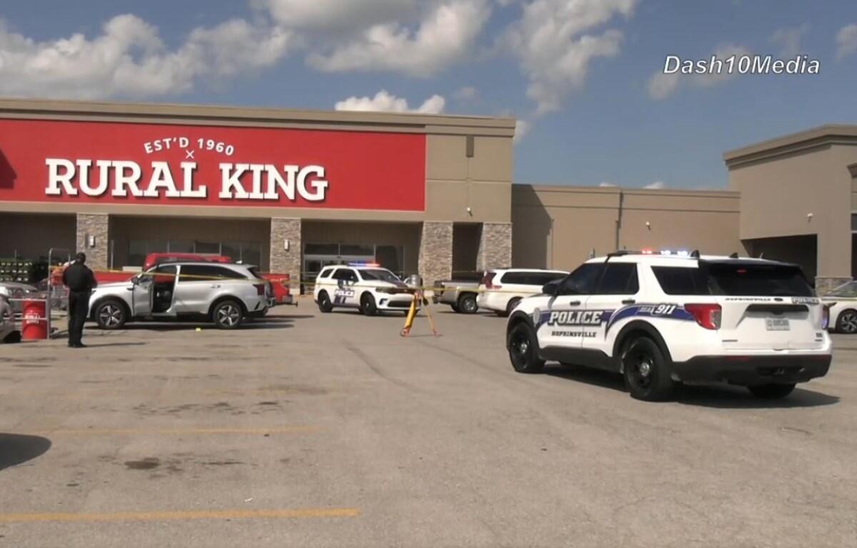 Police cars line the parking lot in front of a Rural King store during an incident, with officers near a white SUV and a barricade in place.