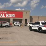 Police cars line the parking lot in front of a Rural King store during an incident, with officers near a white SUV and a barricade in place.