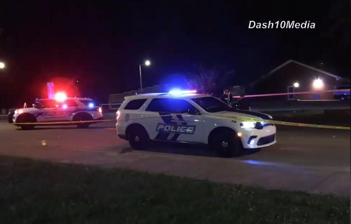 Police cars with flashing blue and red lights on a street at night, yellow tape cordoning off the area.