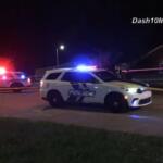 Police cars with flashing blue and red lights on a street at night, yellow tape cordoning off the area.