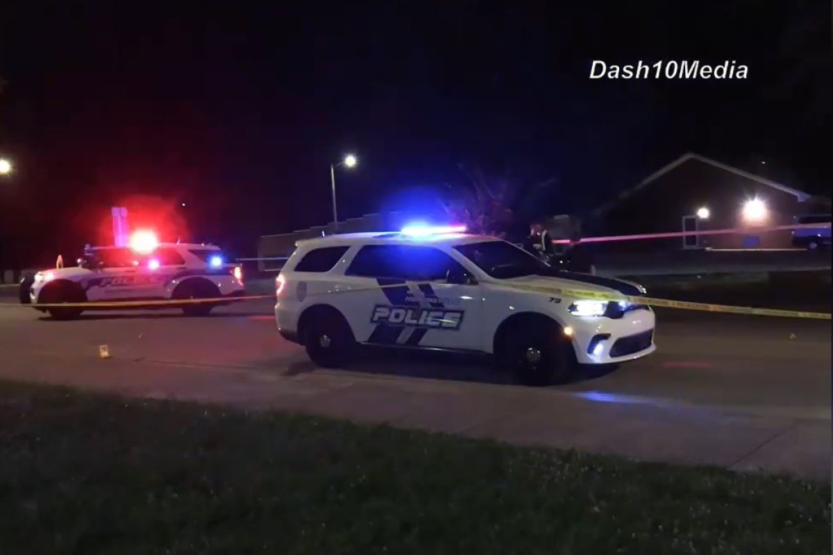 Police cars with flashing blue and red lights on a street at night, yellow tape cordoning off the area.