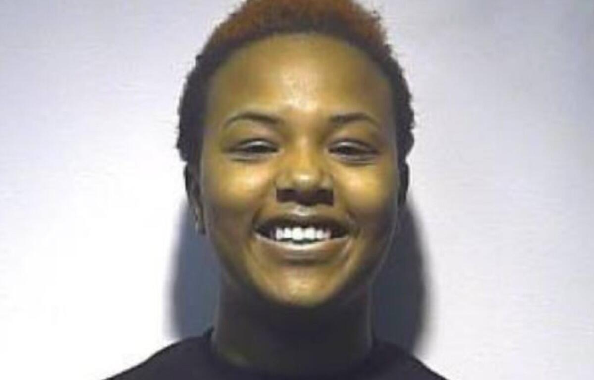 Smiling young woman with short, reddish-brown hair and a dark turtleneck against a light background.