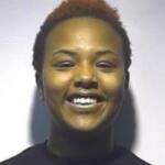 Smiling young woman with short, reddish-brown hair and a dark turtleneck against a light background.