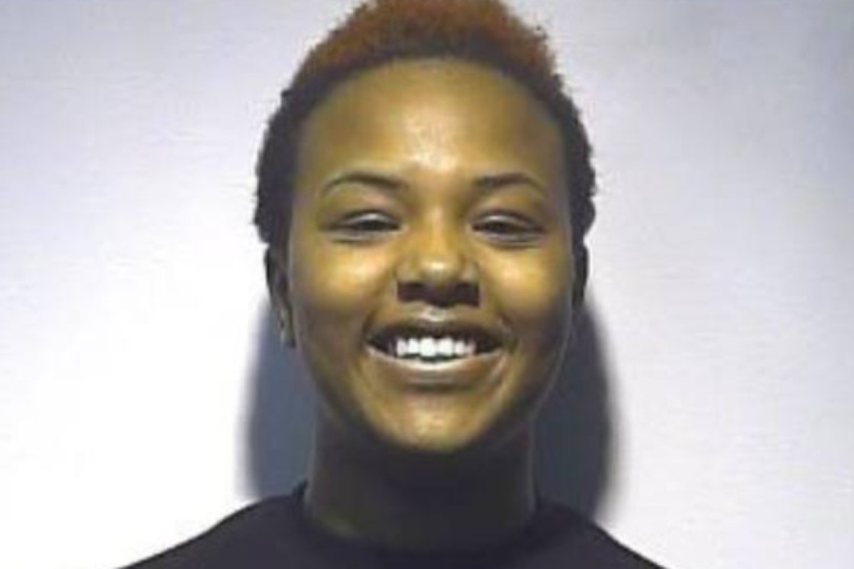 Smiling young woman with short, reddish-brown hair and a dark turtleneck against a light background.
