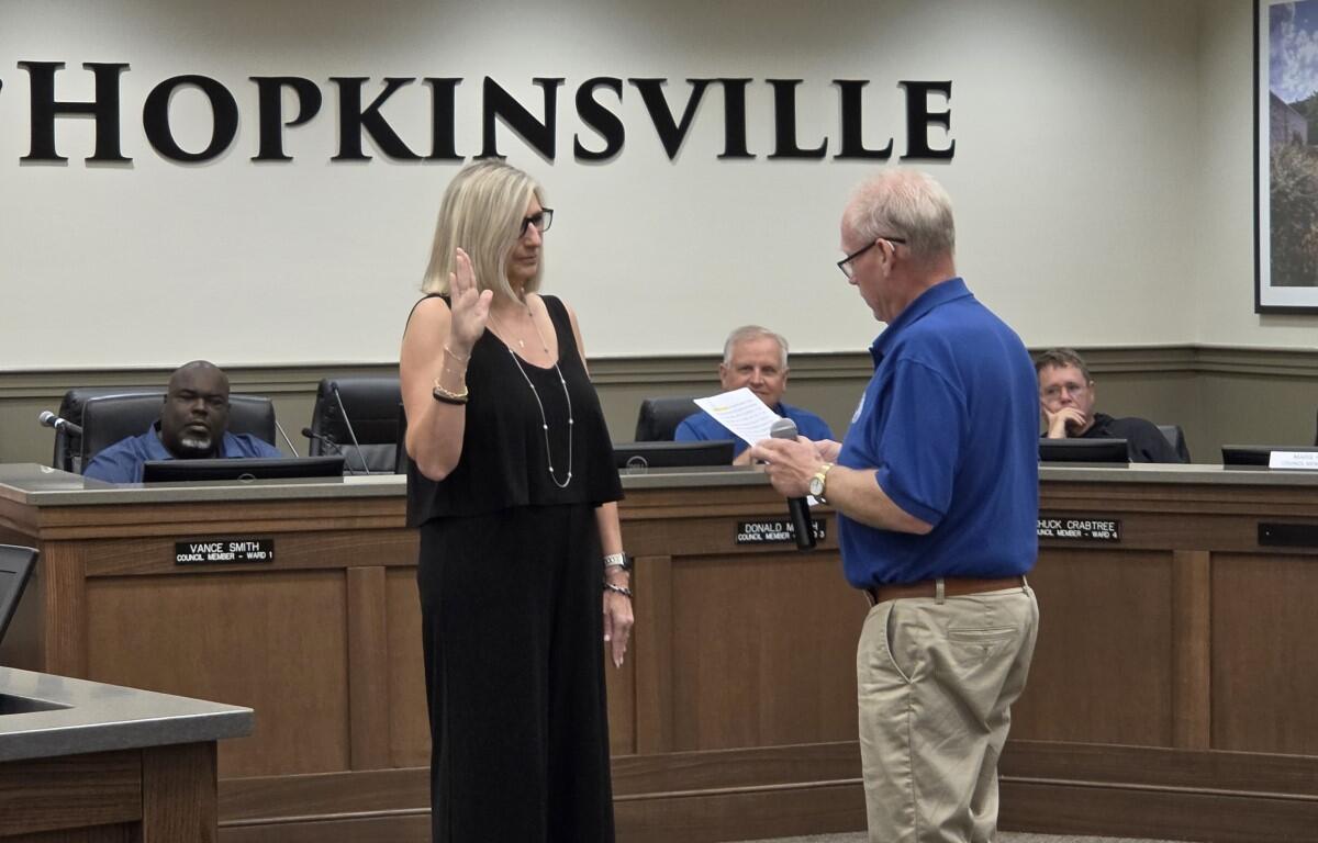 City council chamber scene with a woman raising her right hand as a man reads from a document for an oath ceremony in Hopkinsville courtroom setting