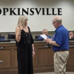 City council chamber scene with a woman raising her right hand as a man reads from a document for an oath ceremony in Hopkinsville courtroom setting