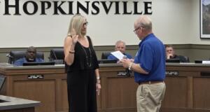 City council chamber scene with a woman raising her right hand as a man reads from a document for an oath ceremony in Hopkinsville courtroom setting
