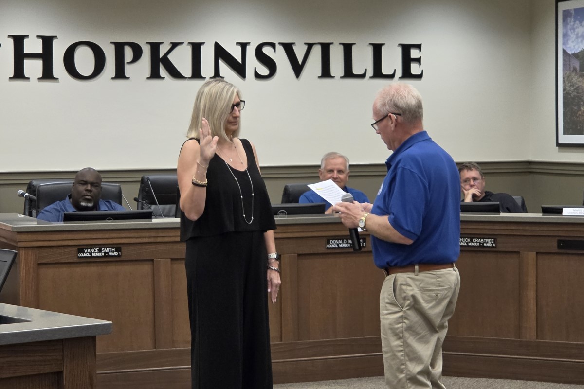 City council chamber scene with a woman raising her right hand as a man reads from a document for an oath ceremony in Hopkinsville courtroom setting