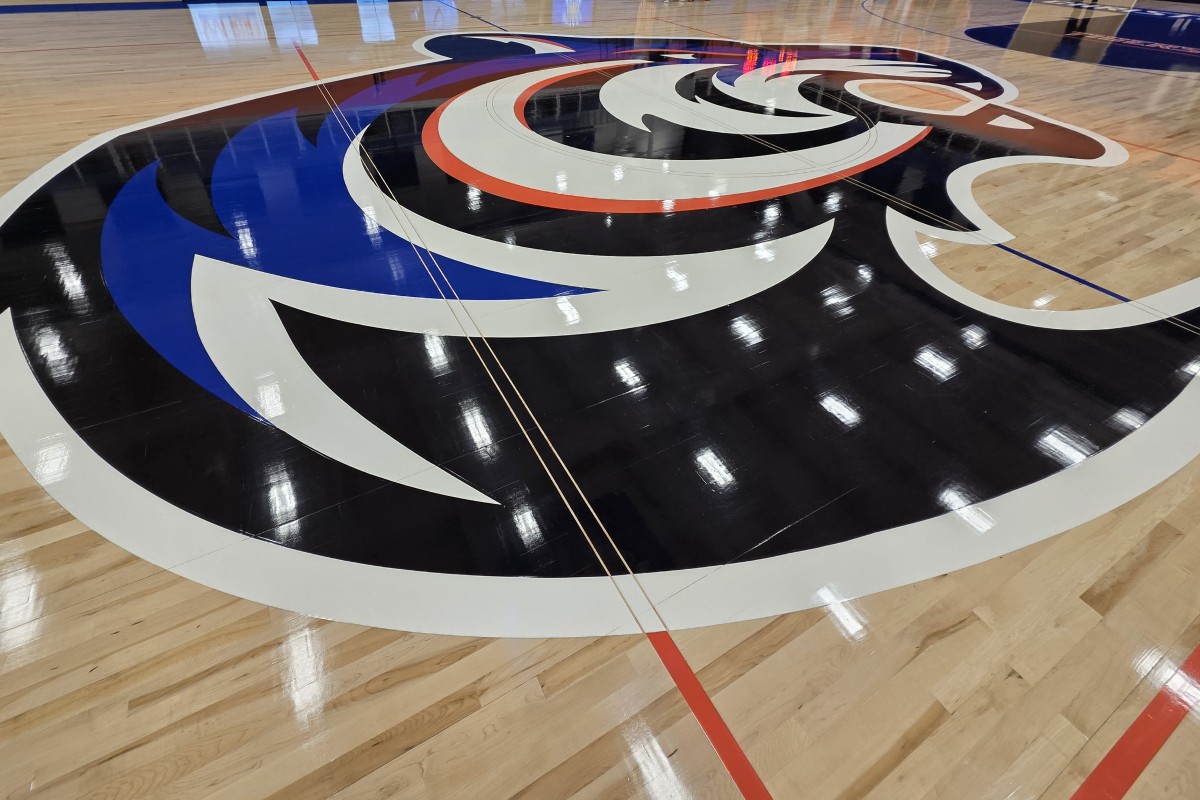 Basketball court floor with a large circular team logo painted at center in black, white, blue, and orange colors.