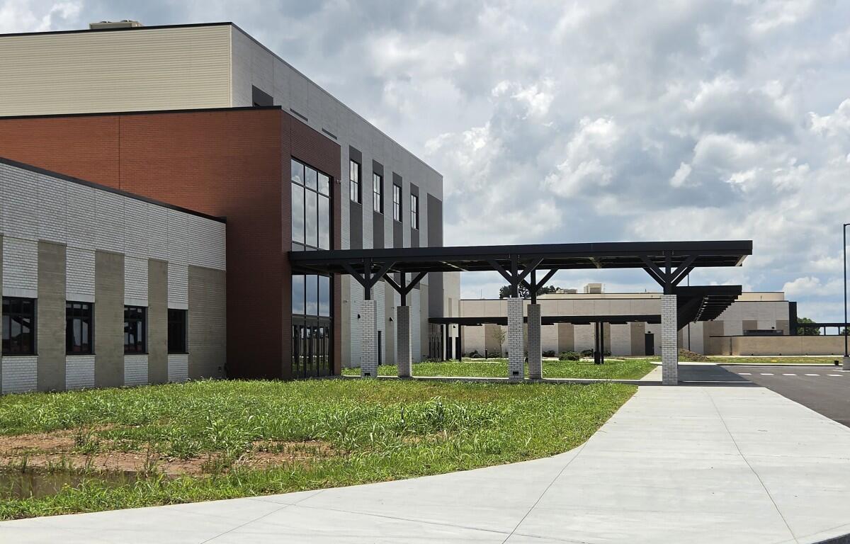 Modern office building with brick and light-colored stone facade, featuring a long covered walkway on concrete columns and a curved concrete path in front.