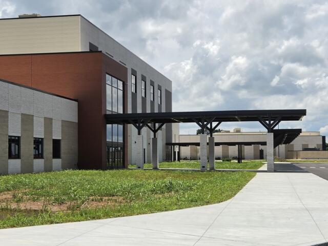Modern office building with brick and light-colored stone facade, featuring a long covered walkway on concrete columns and a curved concrete path in front.