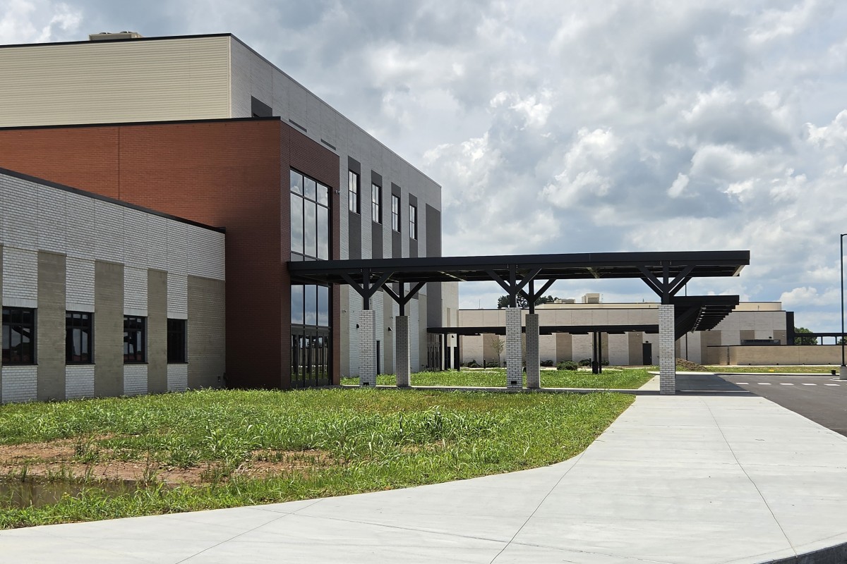 Modern office building with brick and light-colored stone facade, featuring a long covered walkway on concrete columns and a curved concrete path in front.