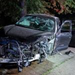 Black Toyota Tundra pickup severely damaged in a nighttime crash; hood crumpled, windshield shattered, doors open beside the road.