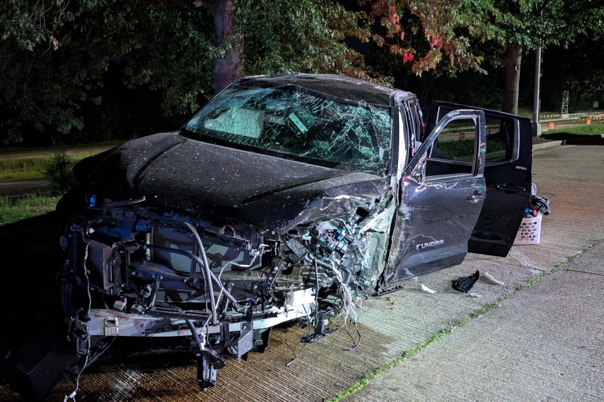 Black Toyota Tundra pickup severely damaged in a nighttime crash; hood crumpled, windshield shattered, doors open beside the road.