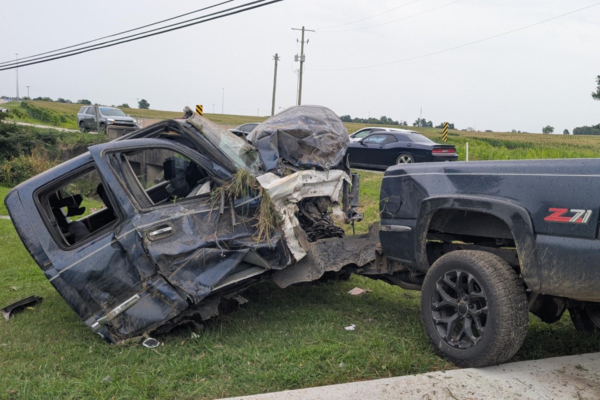 Pickup truck towing a severely damaged SUV on a grassy roadside after a collision, front end crushed and debris scattered nearby.