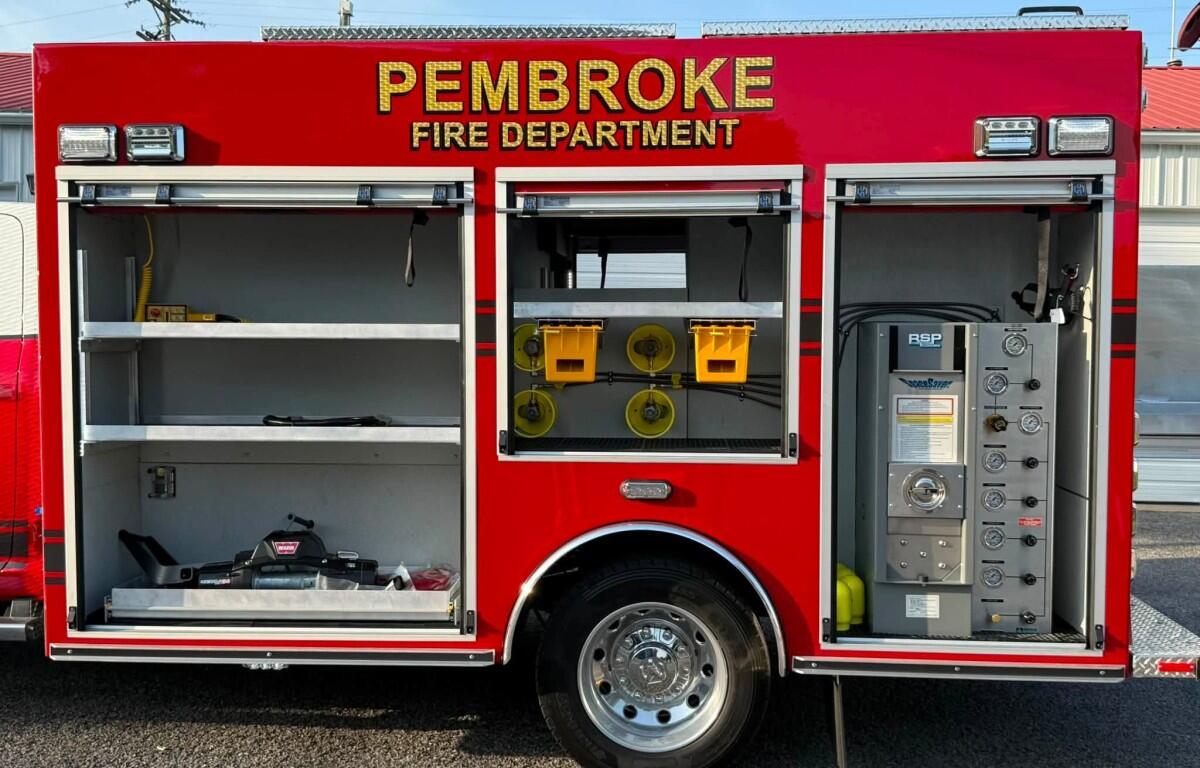 Red Pembroke Fire Department truck side with open compartments showing hoses, tools, and control panel.